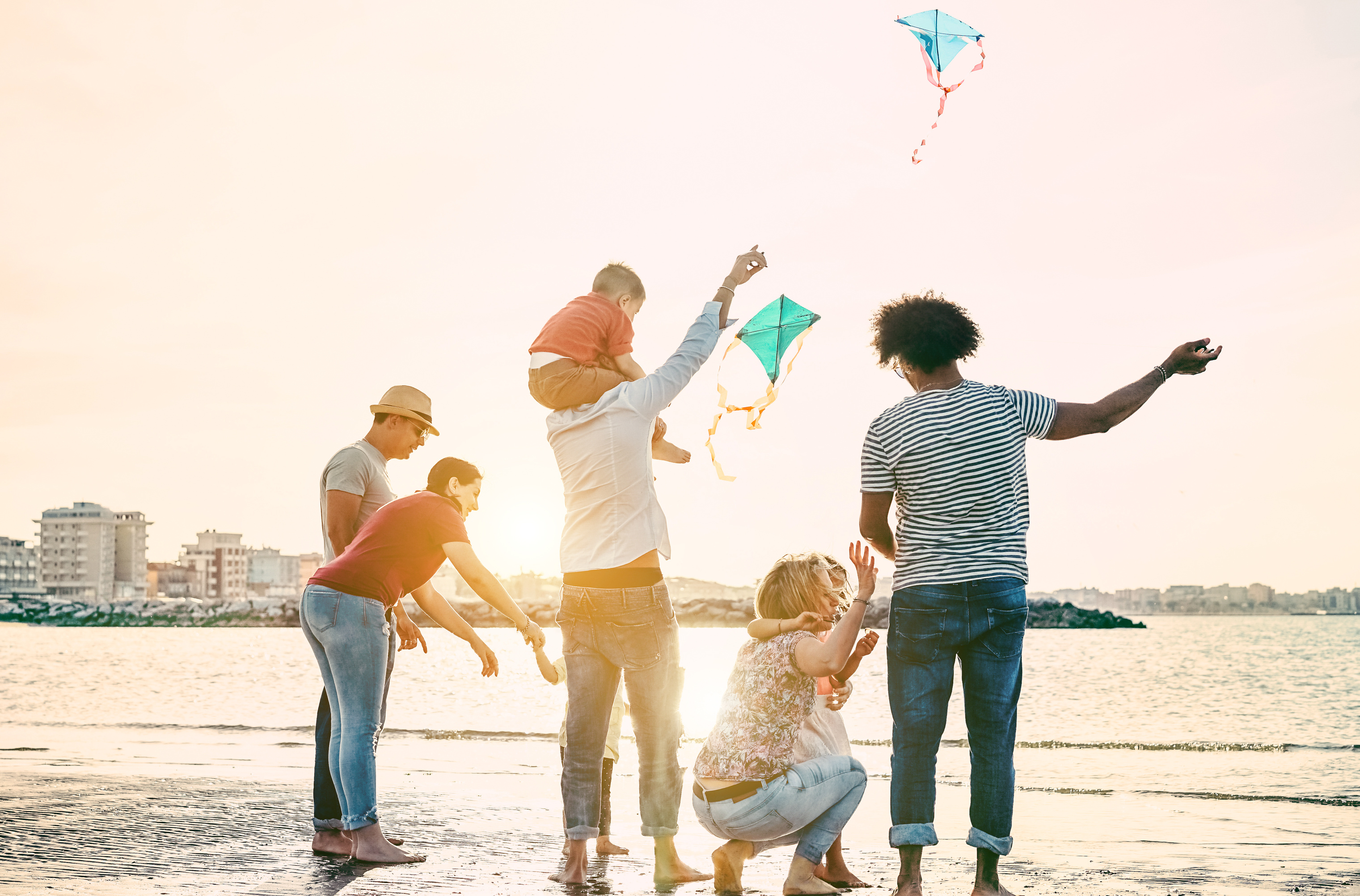 Happy familes flying with kite and having fun on the beach - Parents playing with children outdoor - Travel,love and holidays concept - Main focus on right woman - Warm filter