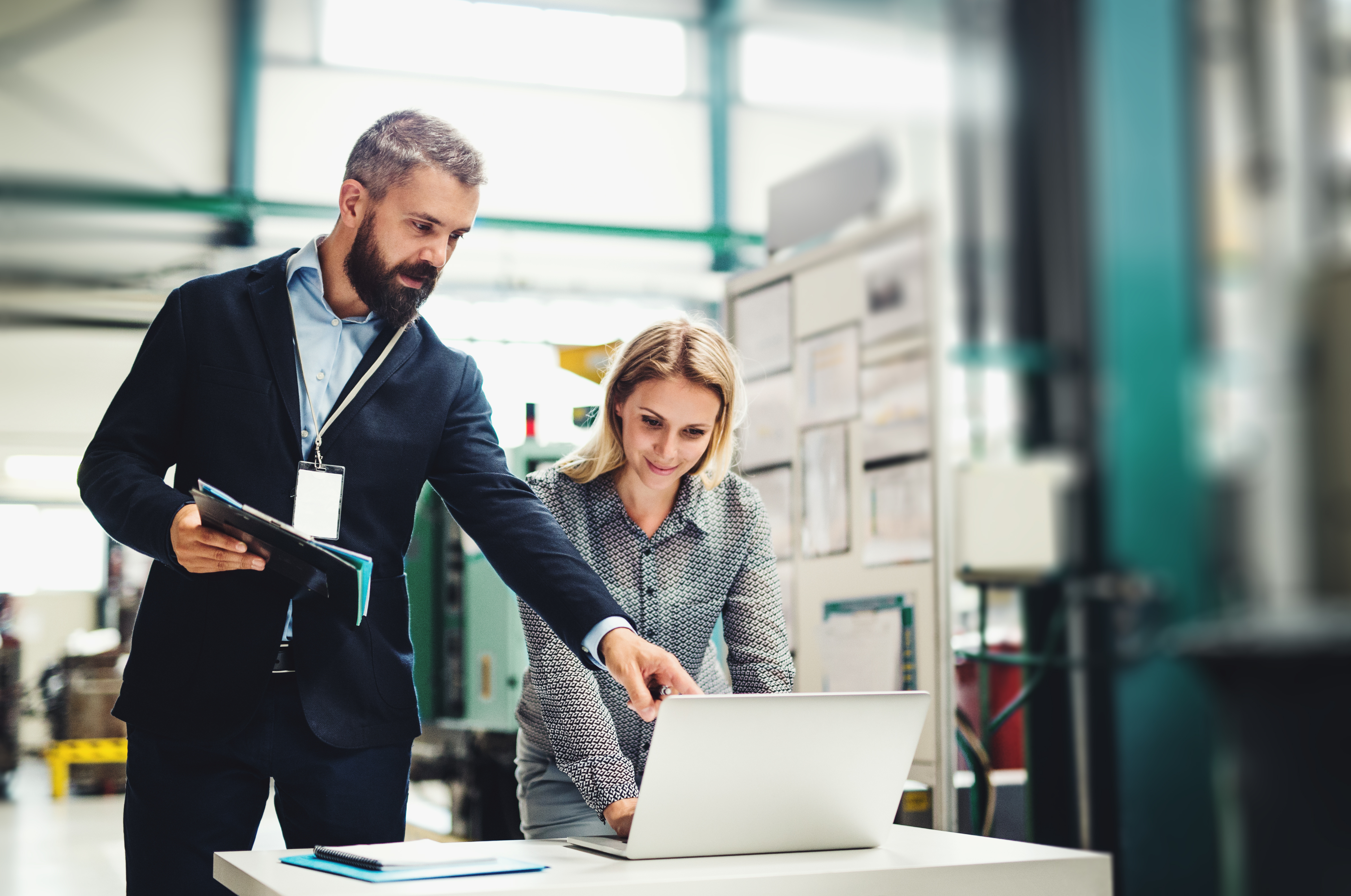 A portrait of an industrial man and woman engineer with laptop in a factory, working.