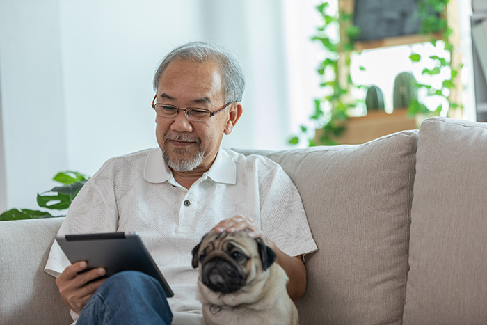 man sitting on sofa and using computer tablet and smile with dog 