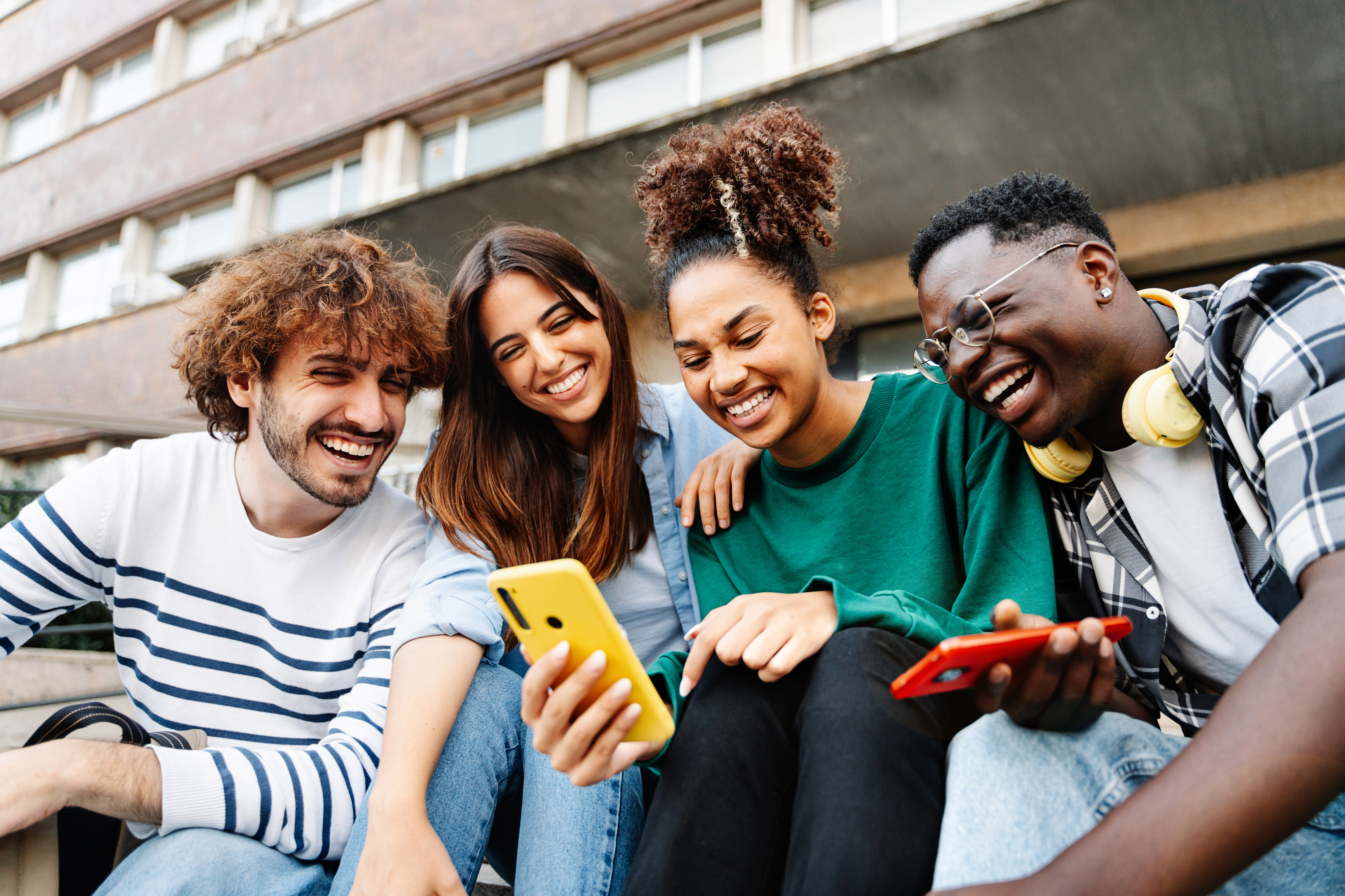 Group of university student friends sitting together using mobile phones to share content on social media