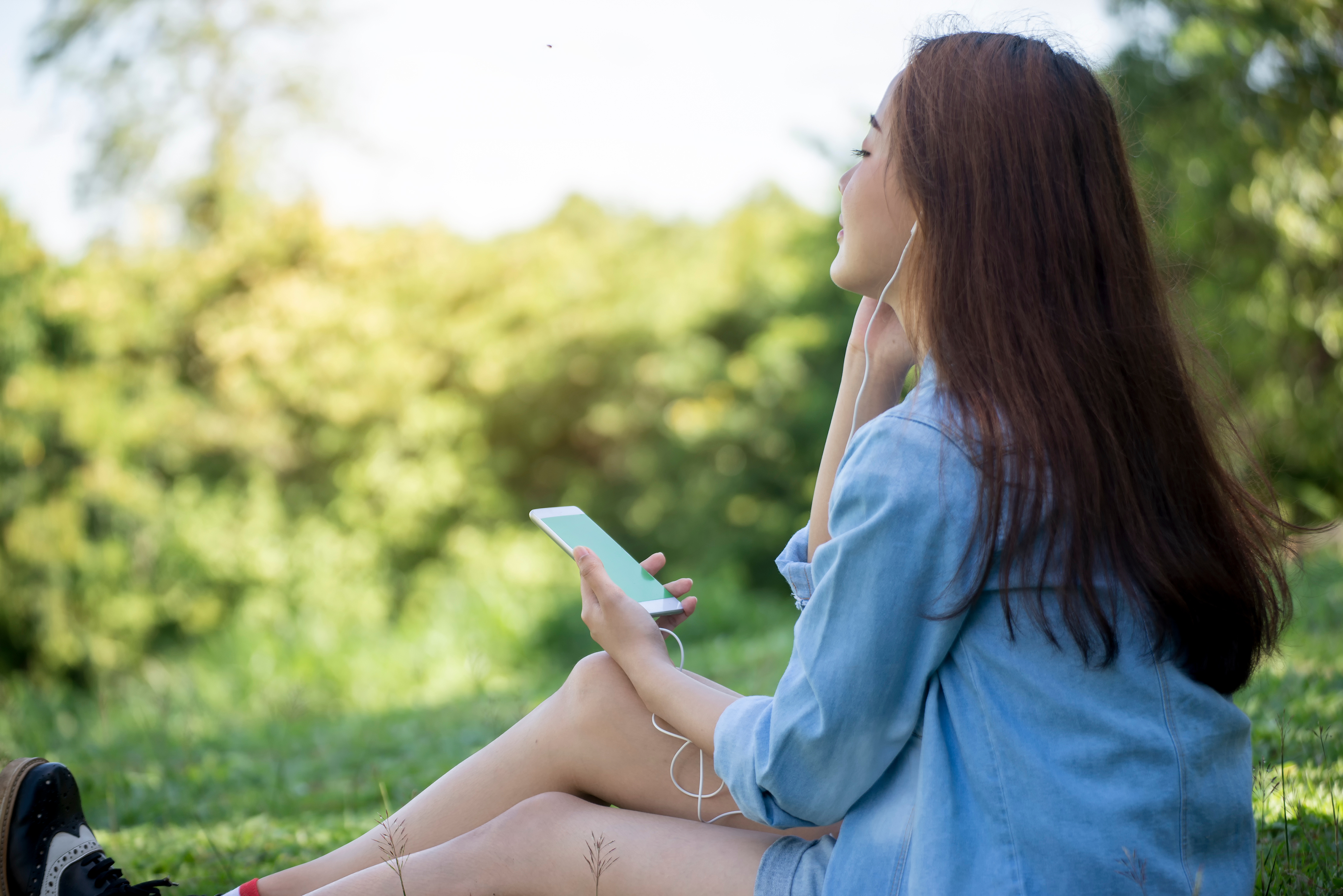 Asain Thai Woman listening to music with earphone of smartphone at nature park. Lifestyle of beautiful Young Girl, sitting and enjoy song outdoor. Lifestyle Concept