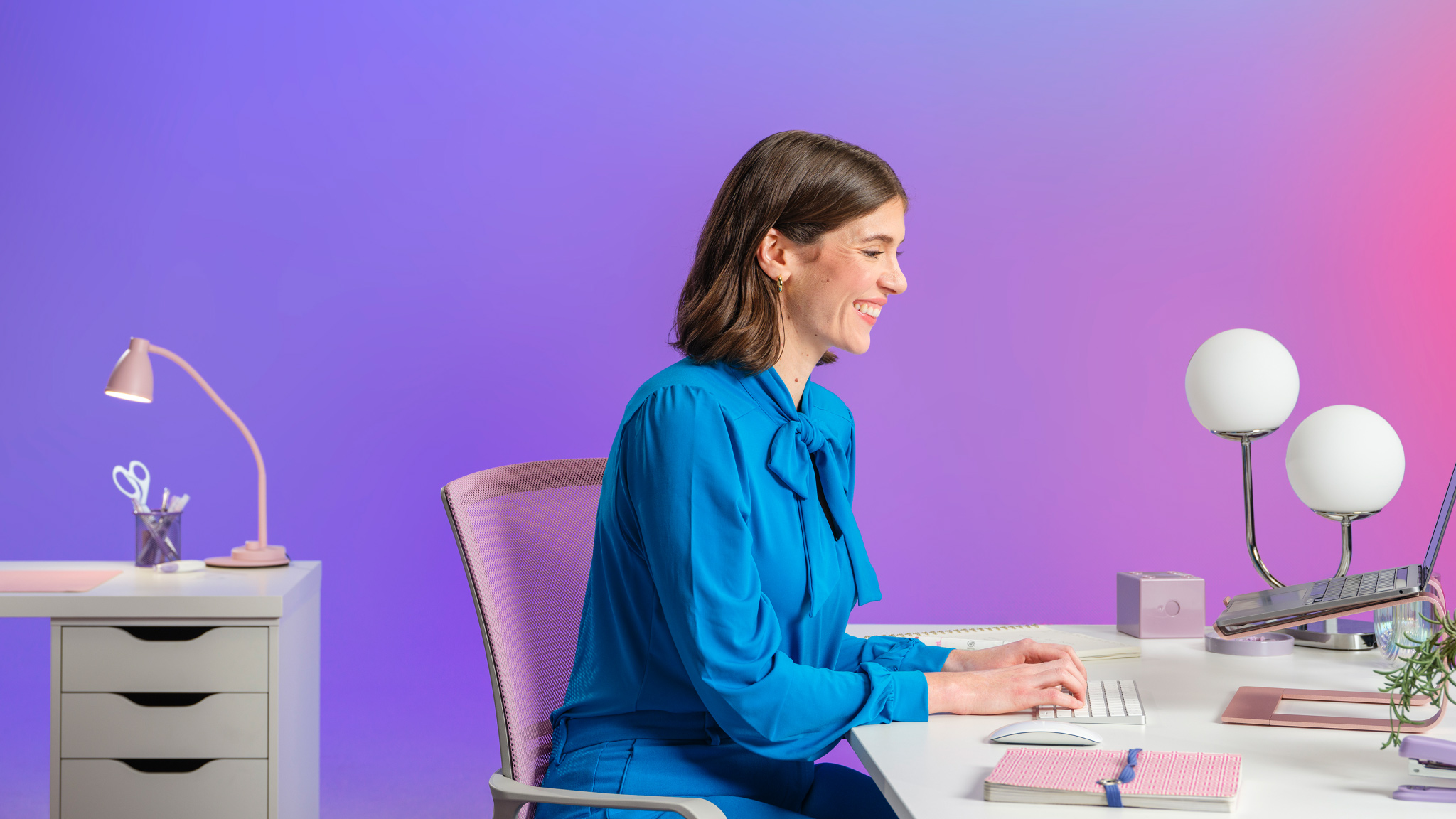 Woman smiling, while sitting at her desk, typing on a wireless keyboard.