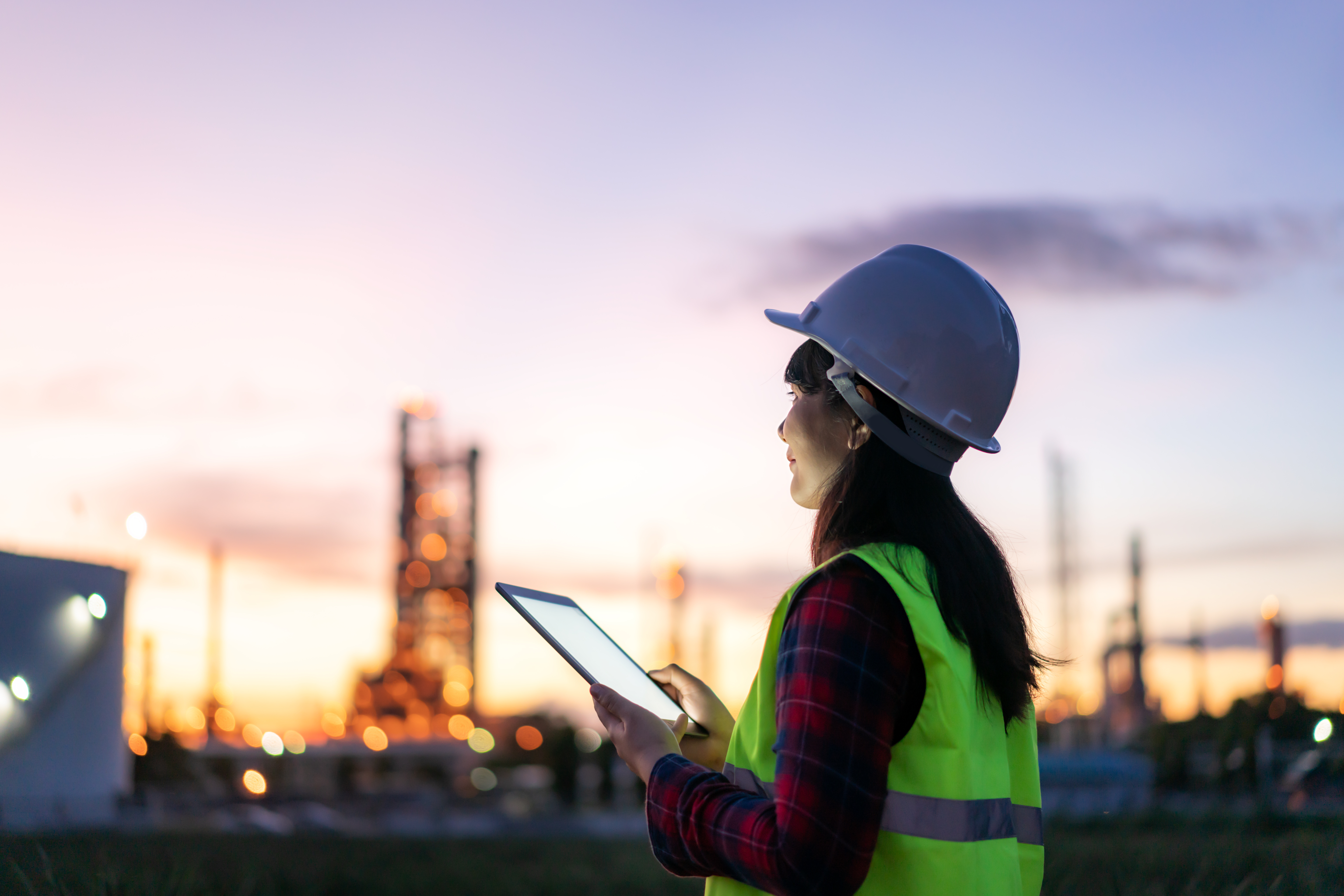 Asian woman petrochemical engineer working at night with digital tablet Inside oil and gas refinery plant industry factory at night for inspector safety quality control.
