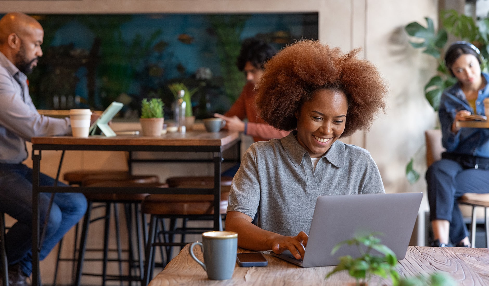 Giovane freelancer sorridente che lavora da un computer portatile in un bar e riceve buone notizie.