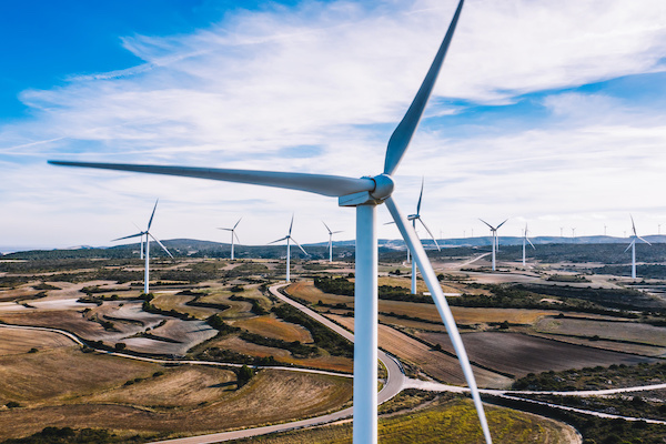 Aerial view of windmills station with rotating propellers generating alternative clean green power from eco resources in rural agri environment.Birds eye view of line of turbines producing electricity