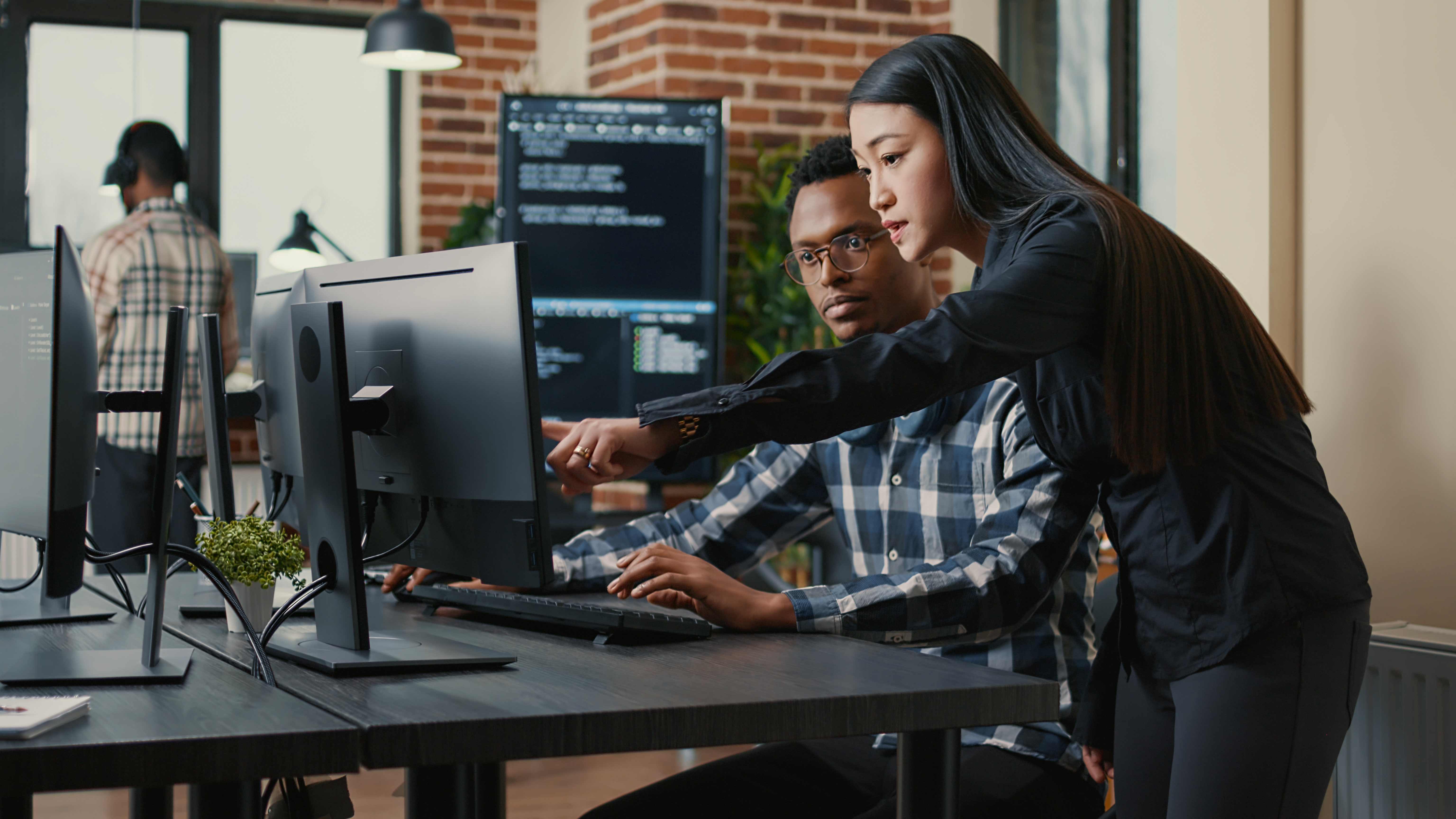 Two programers holding laptop with coding interface walking towards desk and sitting down