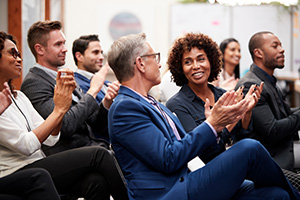 Group Of Businessmen And Businesswomen Applauding Presentation At Conference