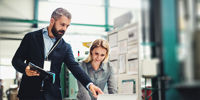 Stock image of two staff members collaborating with a laptop in a factory