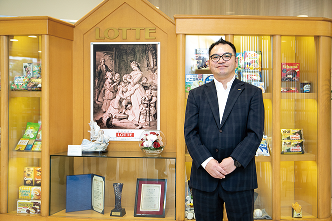 Hisaaki Ogata standing in front of a cabinet of Lotte confectionary