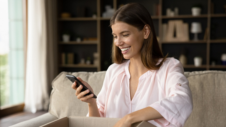 Une femme heureuse d&eacute;balle une bo&icirc;te &agrave; colis, v&eacute;rifie les articles command&eacute;s par t&eacute;l&eacute;phone, utilise une application de commerce &eacute;lectronique au d&eacute;tail, laisse des commentaires positifs au client, se sent satisfaite des marchandises livr&eacute;es, concept de services de livraison rapide