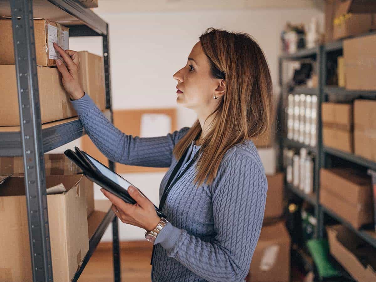 A woman with blonde hair holding a mobile device with a screen and checking the inventory label on a package