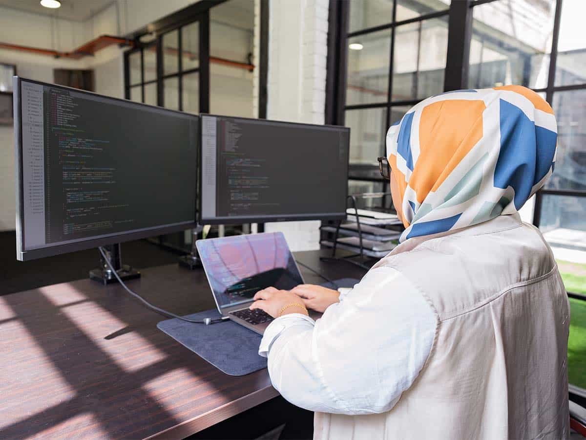 desarrollador escribiendo en una computadora portátil con código en dos monitores