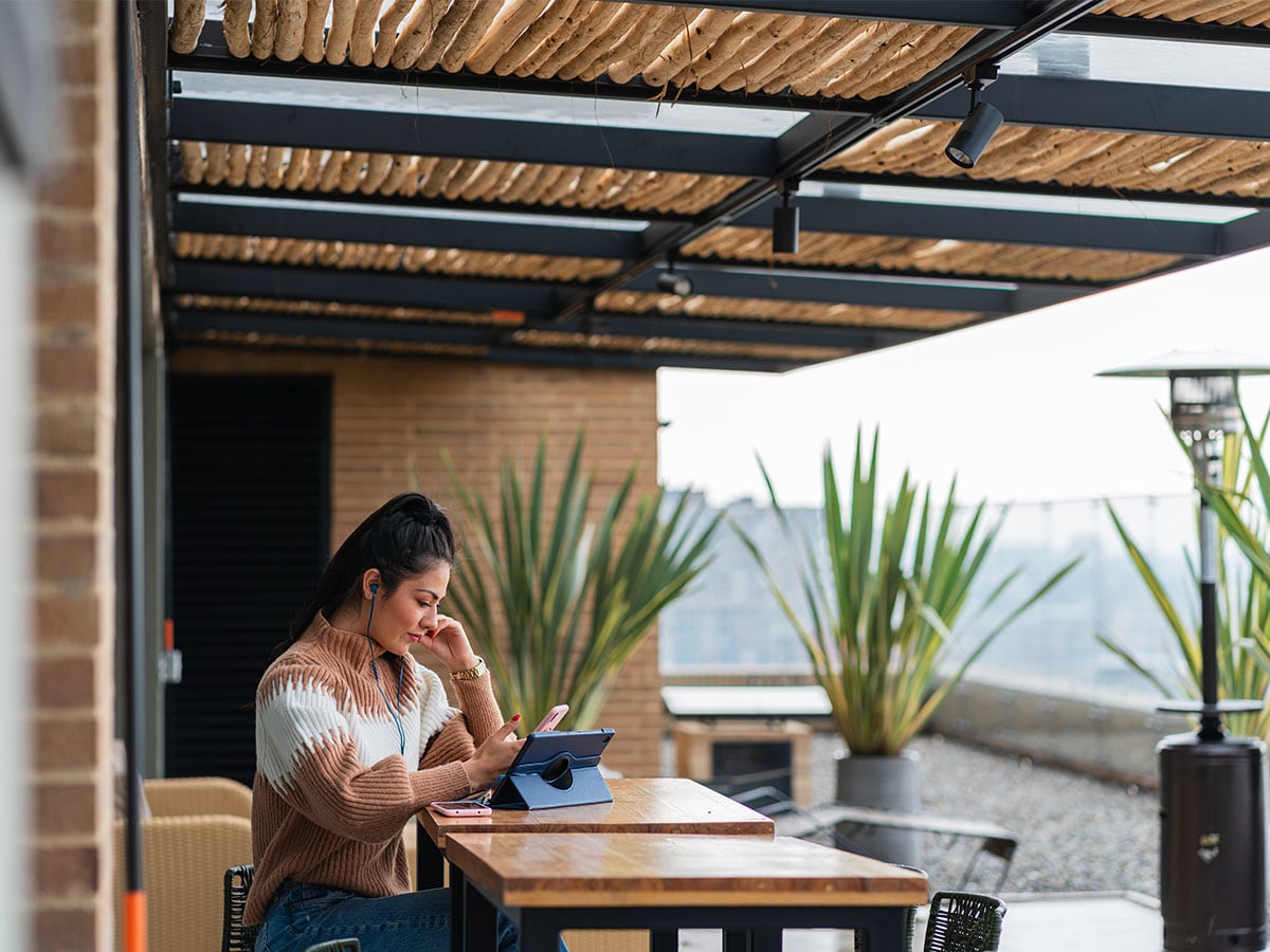 Frau sitzt am Terrassentisch mit Smartphone und Tablet