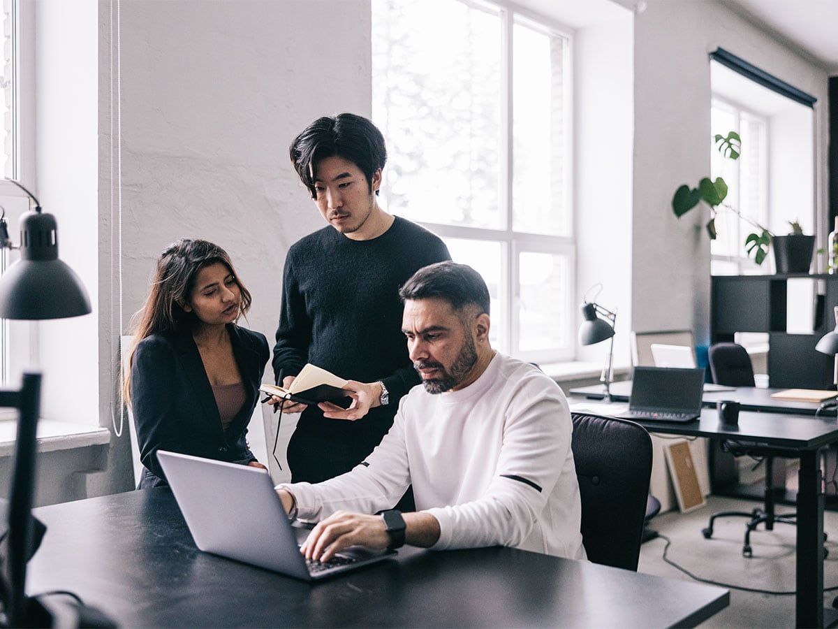 three people at table meeting typing and looking at laptop