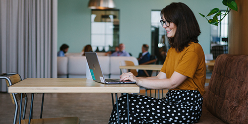 A woman site alone at a desk working on her laptop.