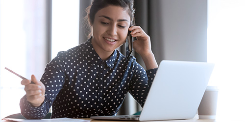 Une employ&eacute;e travaille sur son ordinateur portable tout en parlant au t&eacute;l&eacute;phone.