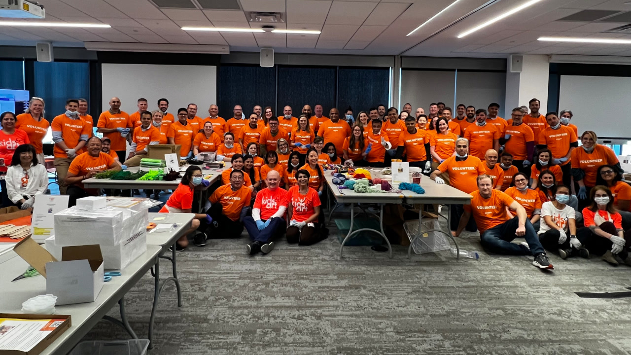 A group photo of about 40 Amazon employees from the AWS Partner Organization Partner Core leadership team at a volunteer event. They're wearing orange Amazon volunteer T-shirts. 