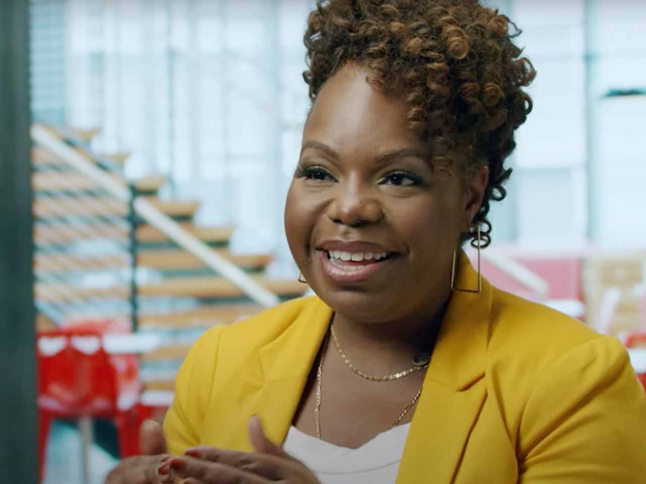 An image of Diya Wynn, head of responsible AI at AWS. She is smiling while talking and looking toward the camera, wearing a yellow blazer with an office setting in the background.