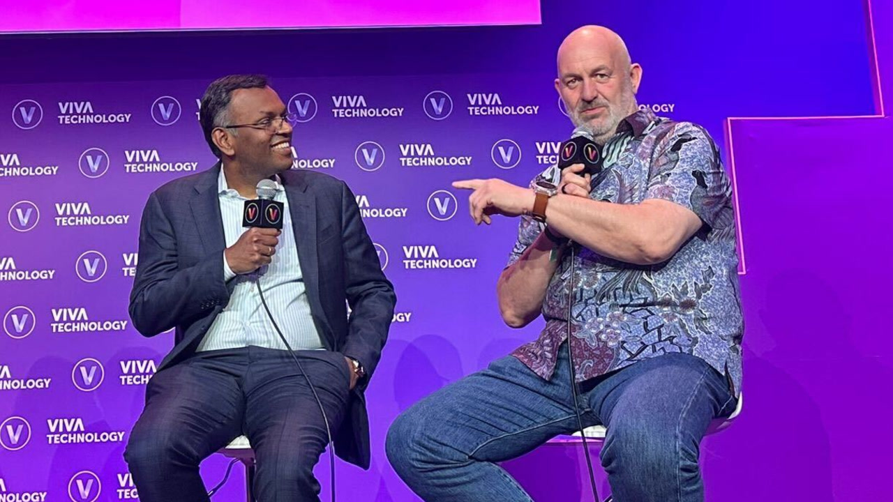 Dr. Swami Sivasubramanian and Dr. Werner Vogels share the stage at the 2024 VivaTech conference in Paris. They're sitting next to each other on stools, both holding microphones, and engaged in conversation. There is a bright purple stage backdrop behind them covered with several Viva Technology logos.