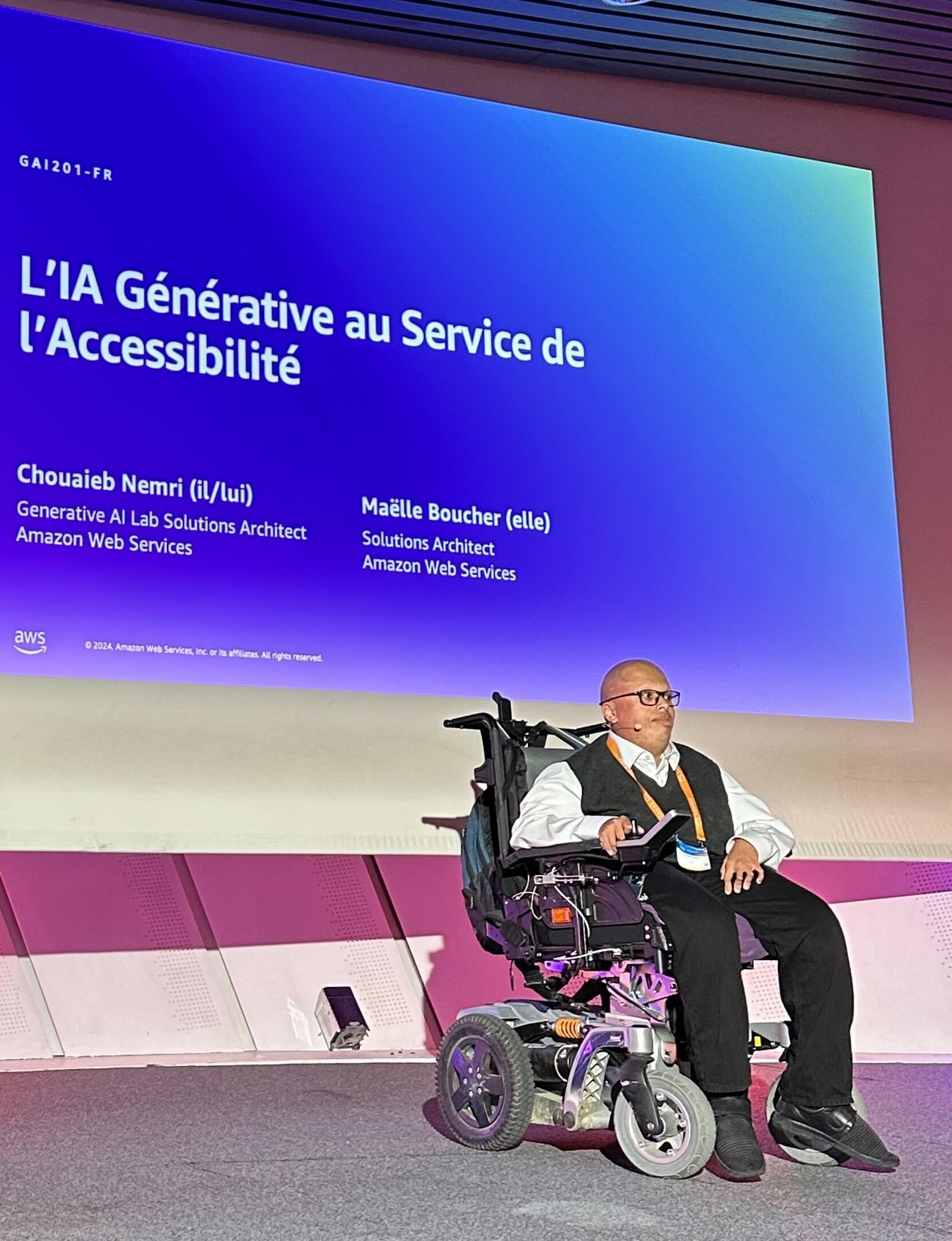 Chouaieb Nemri speaks on stage at the AWS Summit in Paris. Chouaieb has muscular dystrophy and uses a wheelchair.