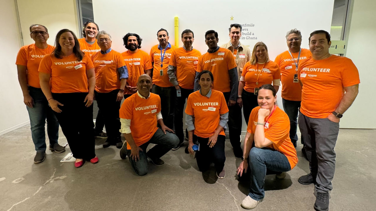 A group of about a dozen Amazon volunteers wearing orange Amazon volunteer T-shirts, after volunteering together to improve career readiness for students. 