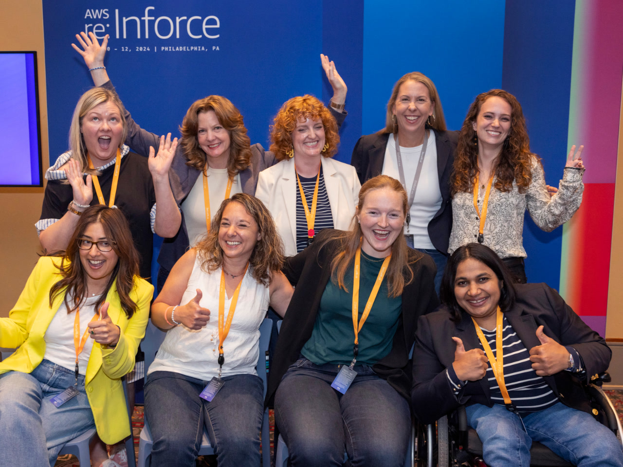 Nine women in security roles at Amazon and AWS smile for a group photo after participating in a panel discussion at AWS re:Inforce. On the wall behind them is an AWS re:Inforce logo.