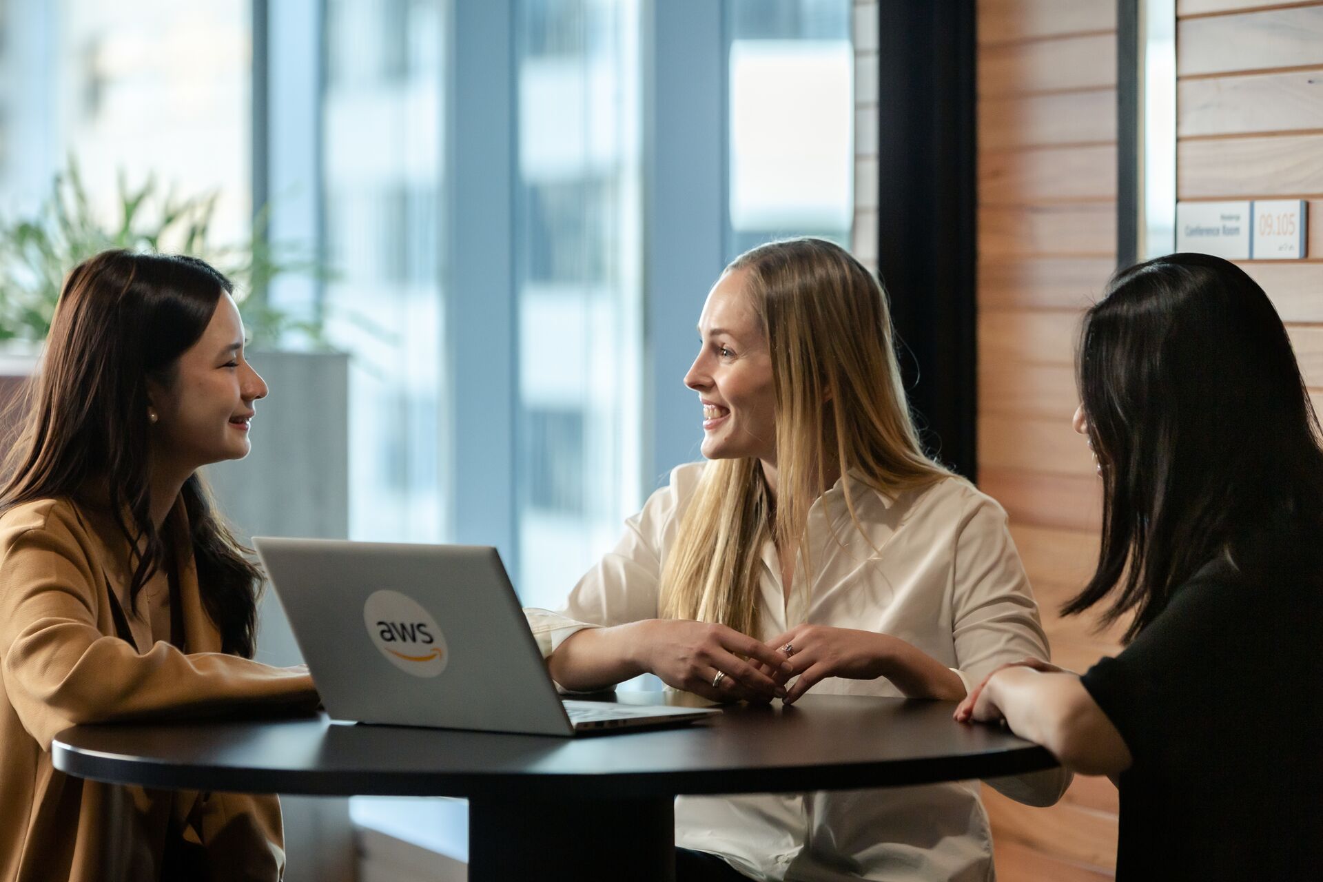 Three AWS employees talking around a table while looking at a laptop.