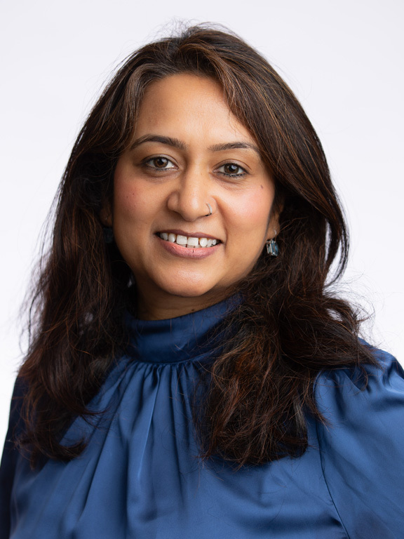 Manisha Mehta, a global employee disability inclusion leader at Amazon. The image is portrait style and shows Manisha smiling, wearing a blue satin blouse.. She presents as a woman of south Asian descent.