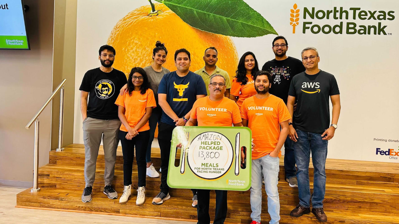 A group of around 10 Amazon employees or volunteers standing together, likely at the North Texas Food Bank facility. They are posing for a photo after packing 13,800 meals, which equates to 16,560 pounds of food, as part of their volunteer effort to support the food bank's mission.