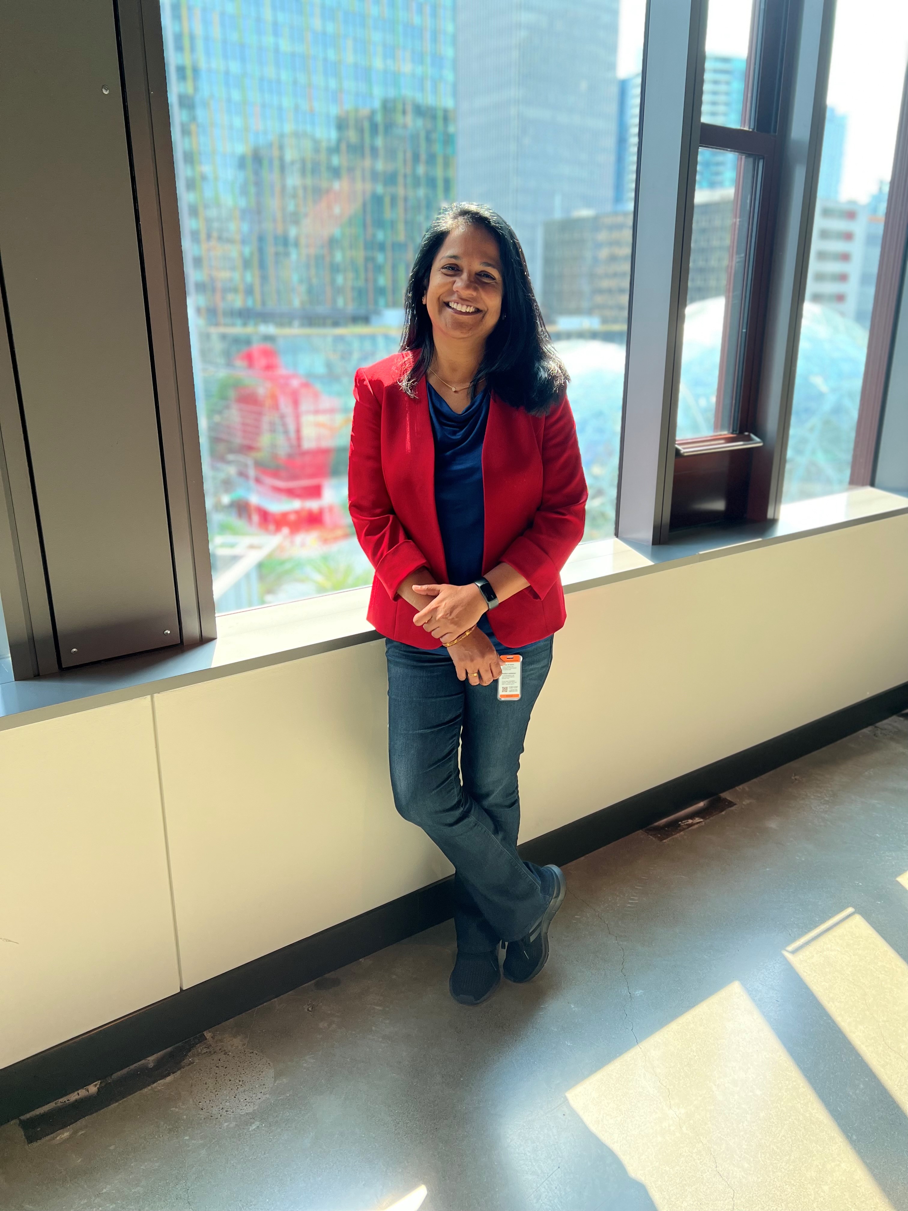 Image of Vanitha Sugumaran, an AWS senior solutions architecture manager, standing in front of a window overlooking the Amazon Spheres in downtown Seattle.