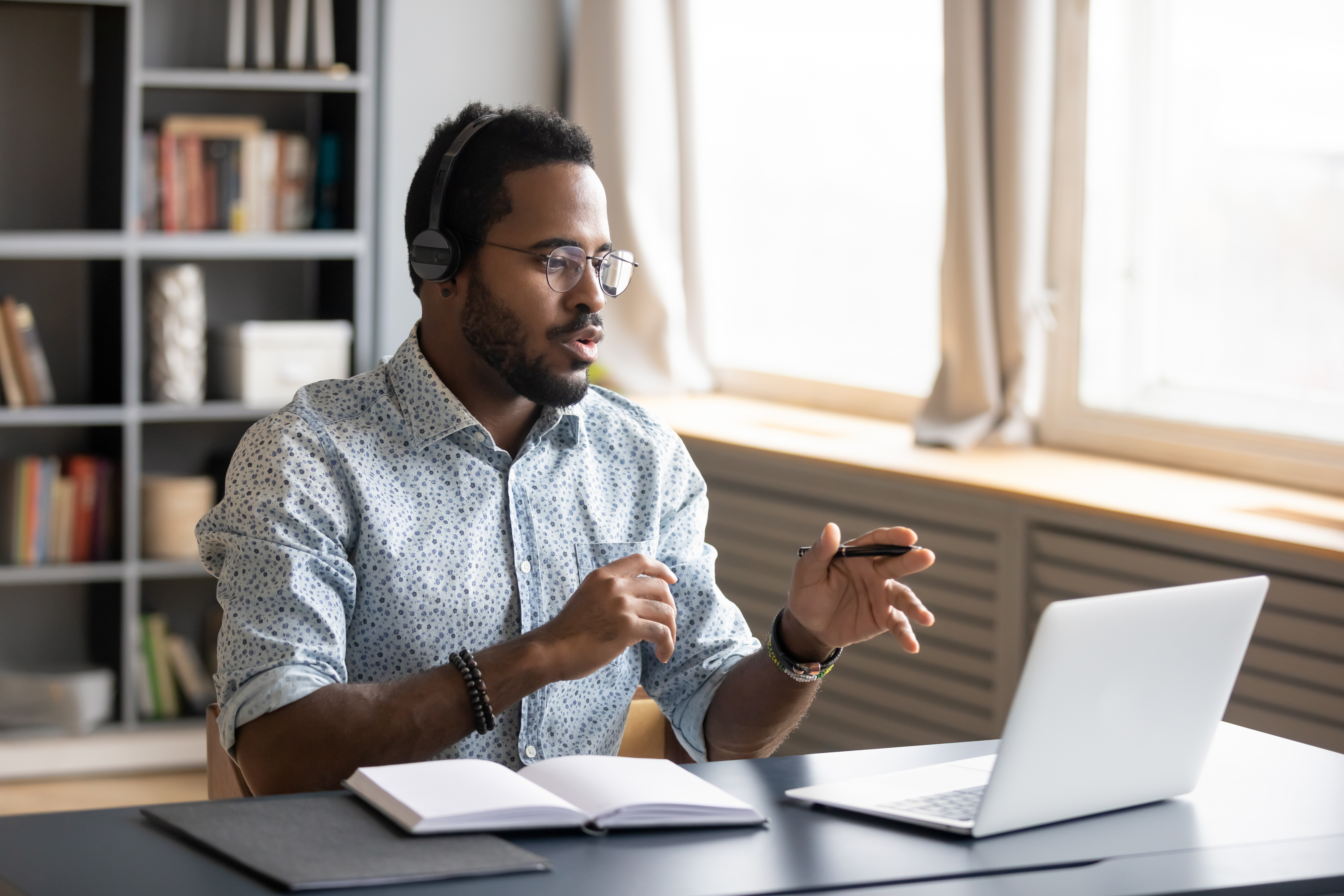 African American man wearing headphones speaking, using laptop