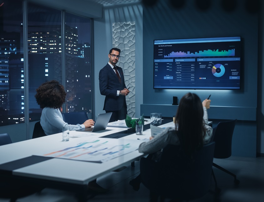 diverse team mates in a conference room meeting regarding data on the presentation screen