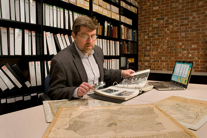 Researcher in archive, searching through maps and photographs