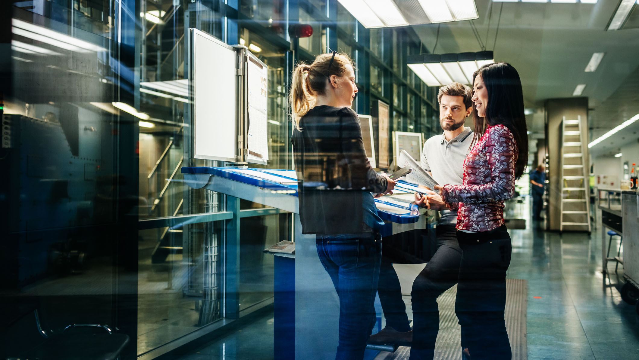 A team of engineers having a discussion at a desk in a large printing factory.