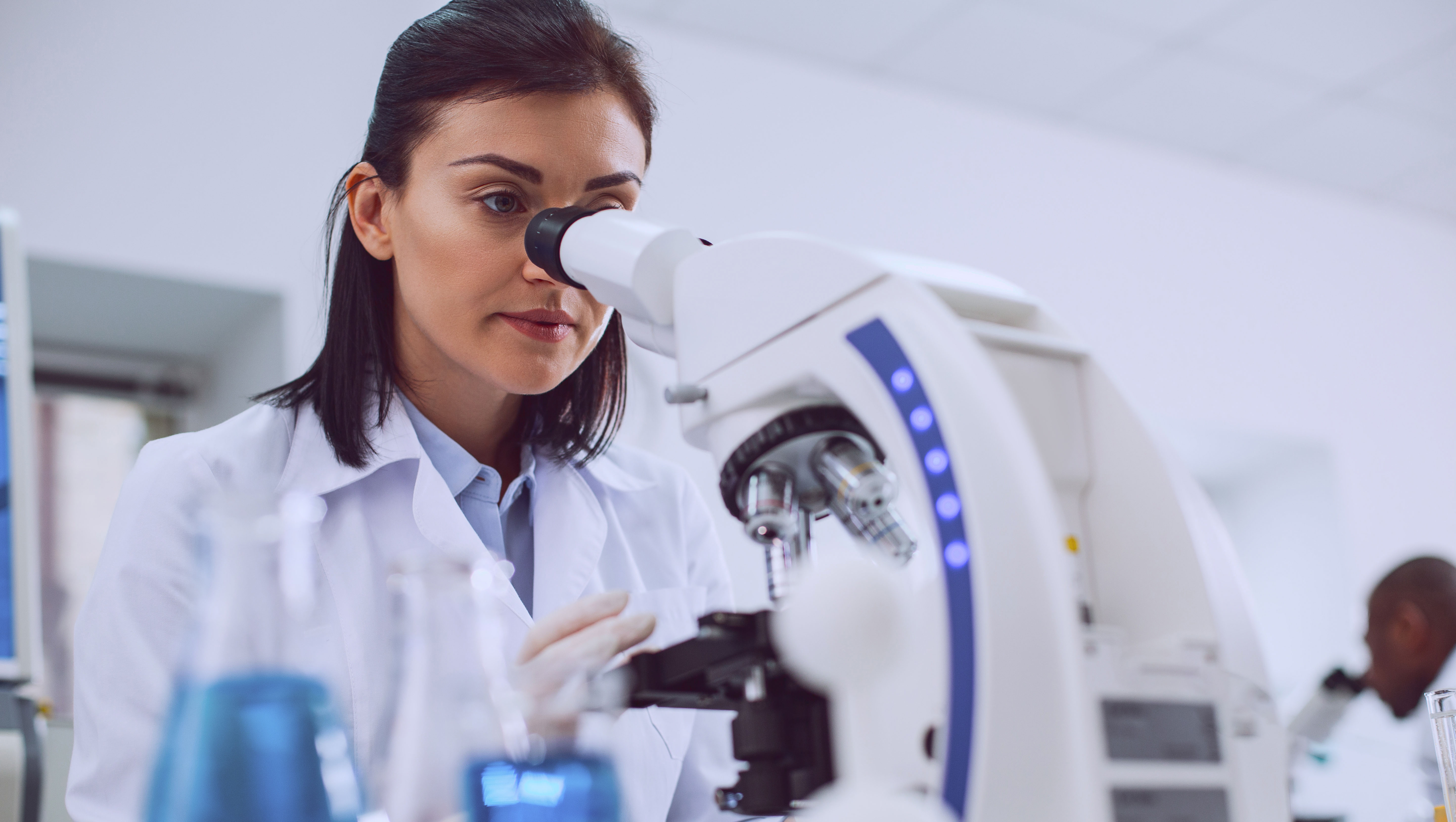 Challenging research. Determined experienced scientist working with her microscope and wearing a uniform