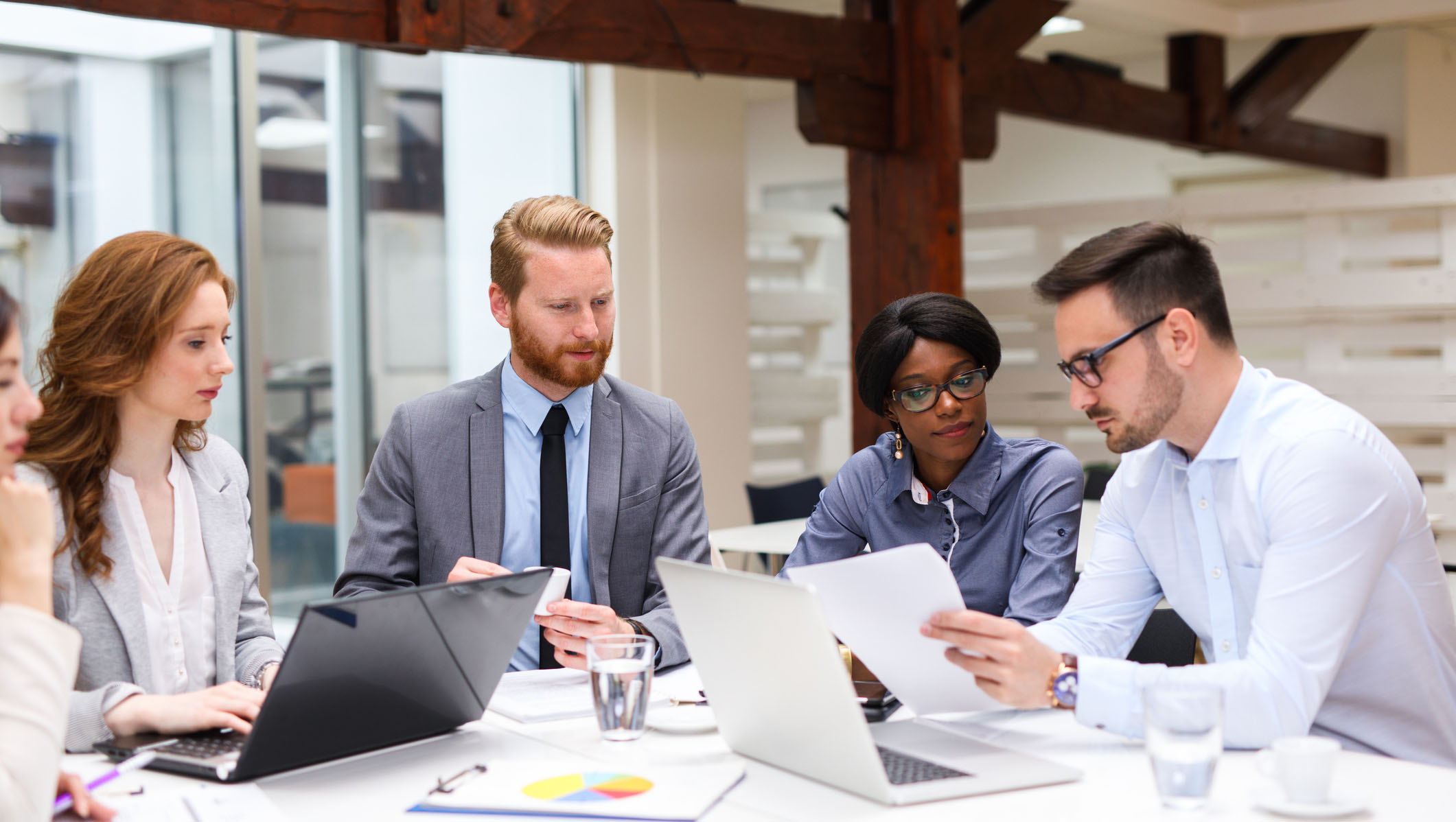 Group of business people is working on new business strategy with a financial analyst while analyzing financial chart during meeting in the office.