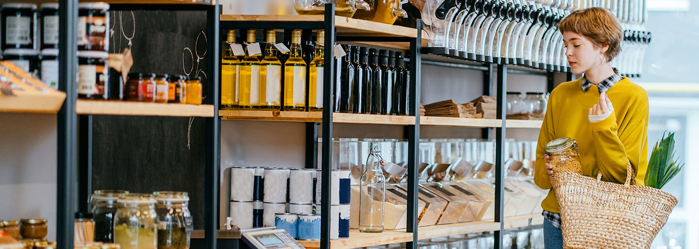 Young Mixed Race Woman Buying Superfoods in Zero Waste Shop. Lots of Healthy Food in Glass Bottles on Stand in Grocery Store. No plastic Conscious Minimalism Vegan Lifestyle Concept.