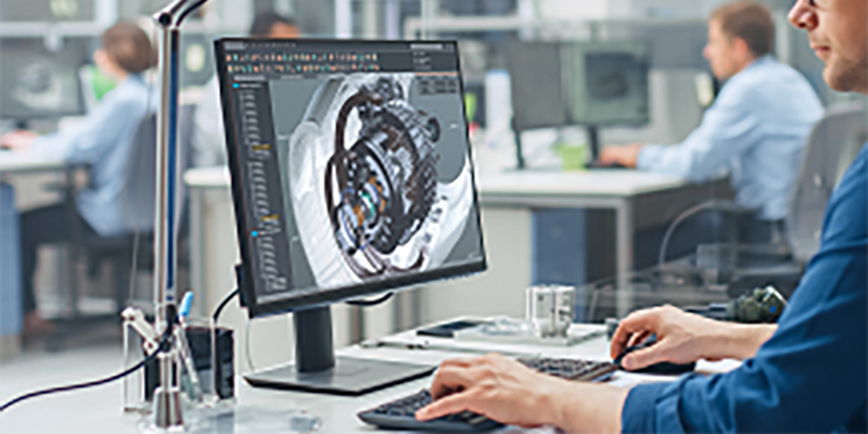 Over the Shoulder Shot of Engineer Working with CAD Software on Desktop Computer, Screen Shows Technical Details and Drawings. In the Background Engineering Facility Specialising on Industrial Design