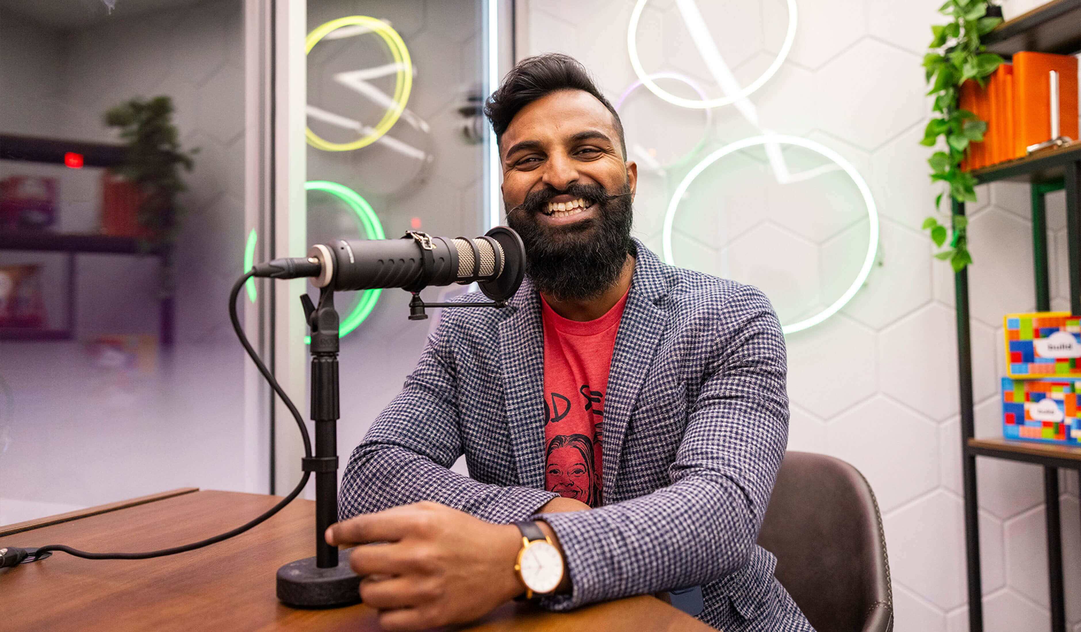 homme derrière un microphone souriant à la caméra dans un studio d’enregistrement