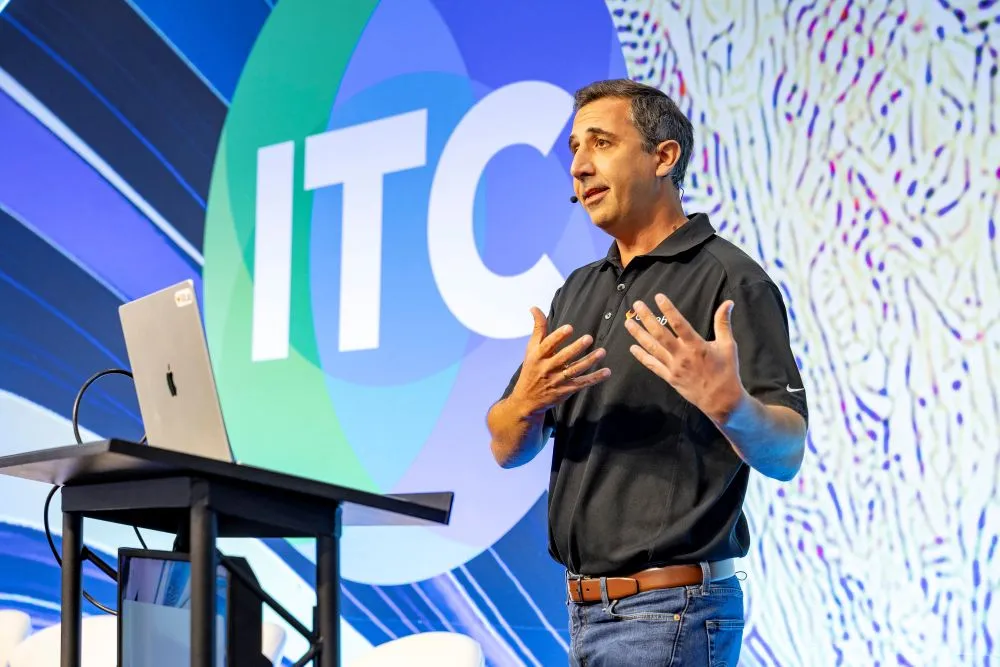 A speaker presents on stage at ITC Vegas in front of a large ITC logo backdrop.