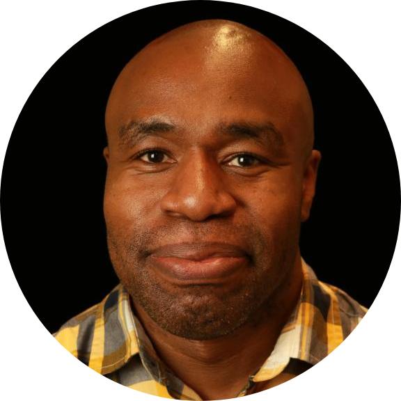 Portrait of a smiling man wearing a yellow plaid shirt with a black background.