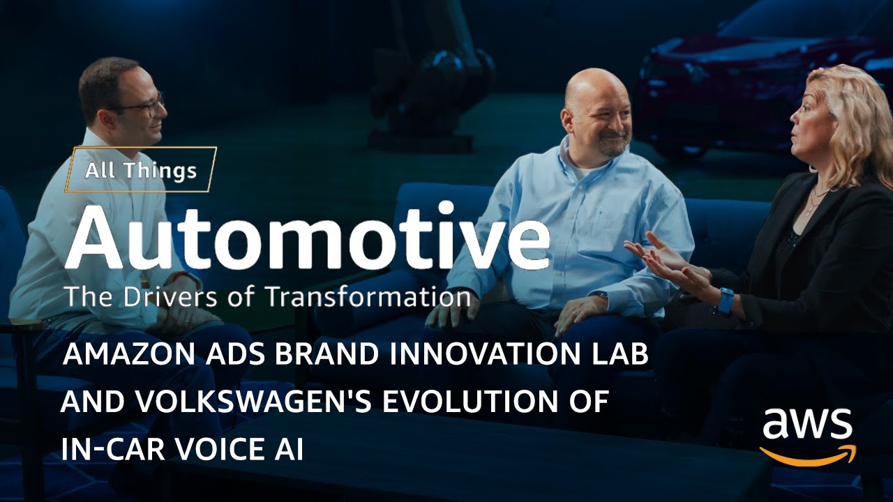 YouTube thumbnail image showing three people seated and talking with the overlaid text: 'All Things Automotive: The Drivers of Transformation. Amazon Ads Brand Innovation Lab and Volkswagen's Evolution of In-Car Voice AI.' AWS logo appears in the corner. The setting is studio-like, intended for a discussion on automotive technology and in-car voice AI.