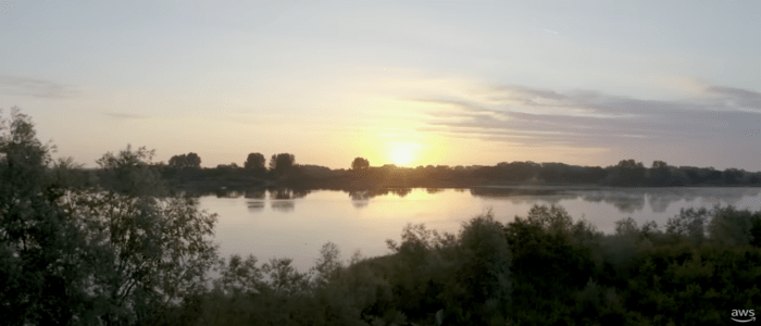 Sunrise over a calm lake with trees in the foreground, promoting AWS sustainability.