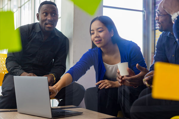 A group of people collaborating around a laptop, with one person pointing at the screen and another holding a cup.