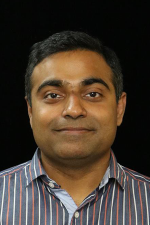 Portrait photo of an author in front of a plain dark background, wearing a striped shirt and looking at the camera.