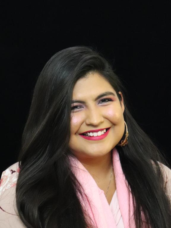 Professional portrait of a woman with long dark hair, wearing a light pink scarf, smiling against a black background.