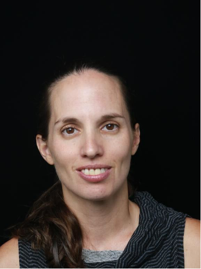 Professional portrait of a woman with long brown hair, wearing a sleeveless top, photographed against a dark background.