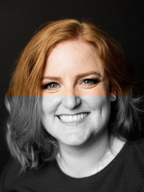 A person with shoulder-length red hair wearing a green top and a gold necklace, set against a dark background.