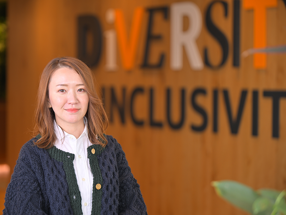 A woman stands in front of a wall with the words 'Diversity Inclusivity' displayed, representing a workplace commitment to diversity and inclusion.