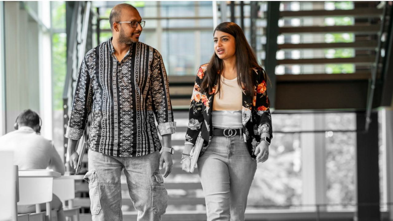 Two coworkers walking and talking in an Amazon office, each carrying laptops, in a bright and modern workspace.